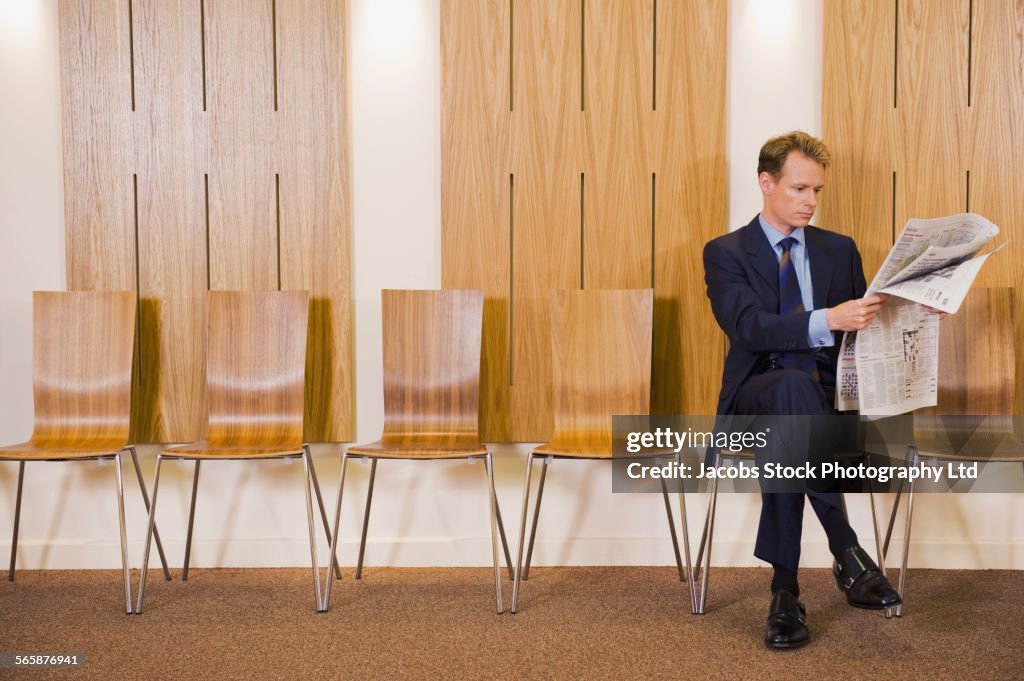 Caucasian businessman reading newspaper in waiting area