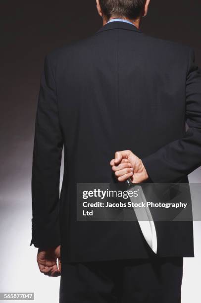 caucasian businessman hiding dagger behind back - dagger stock pictures, royalty-free photos & images