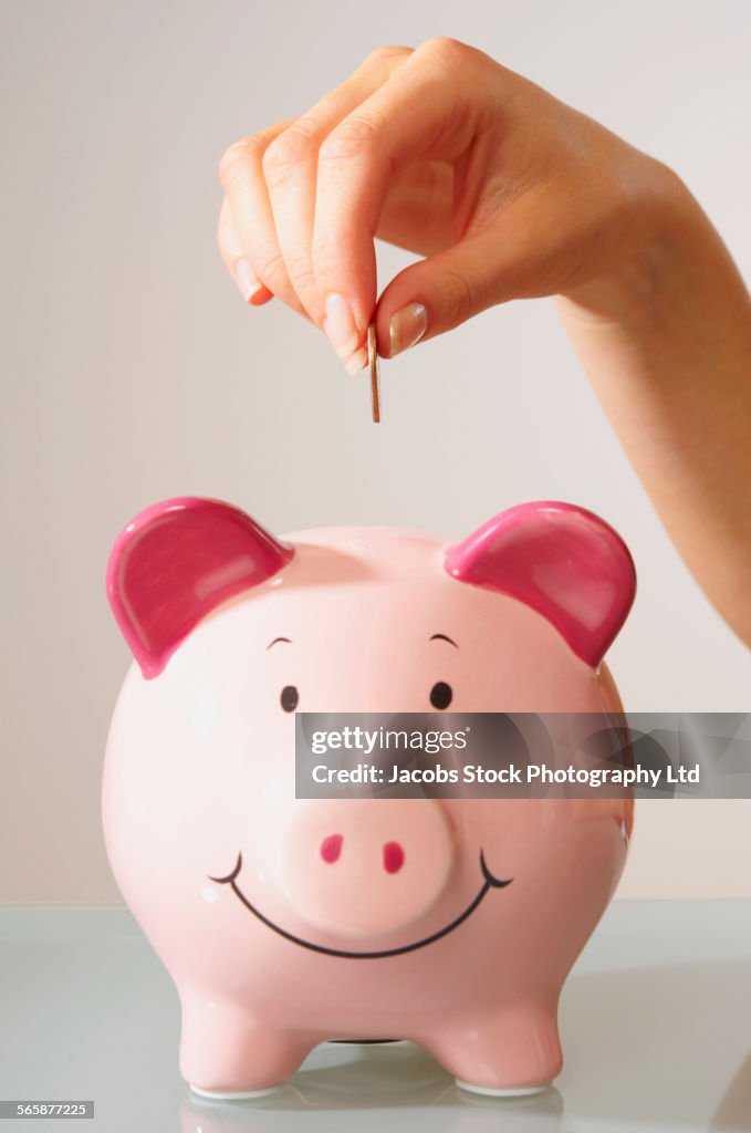 Caucasian woman depositing coin in piggy bank