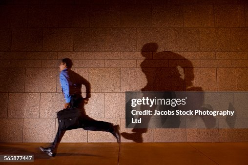 Hispanic businessman running in spotlight on city sidewalk at night Hispanic businessman running in spotlight on city sidewalk at night