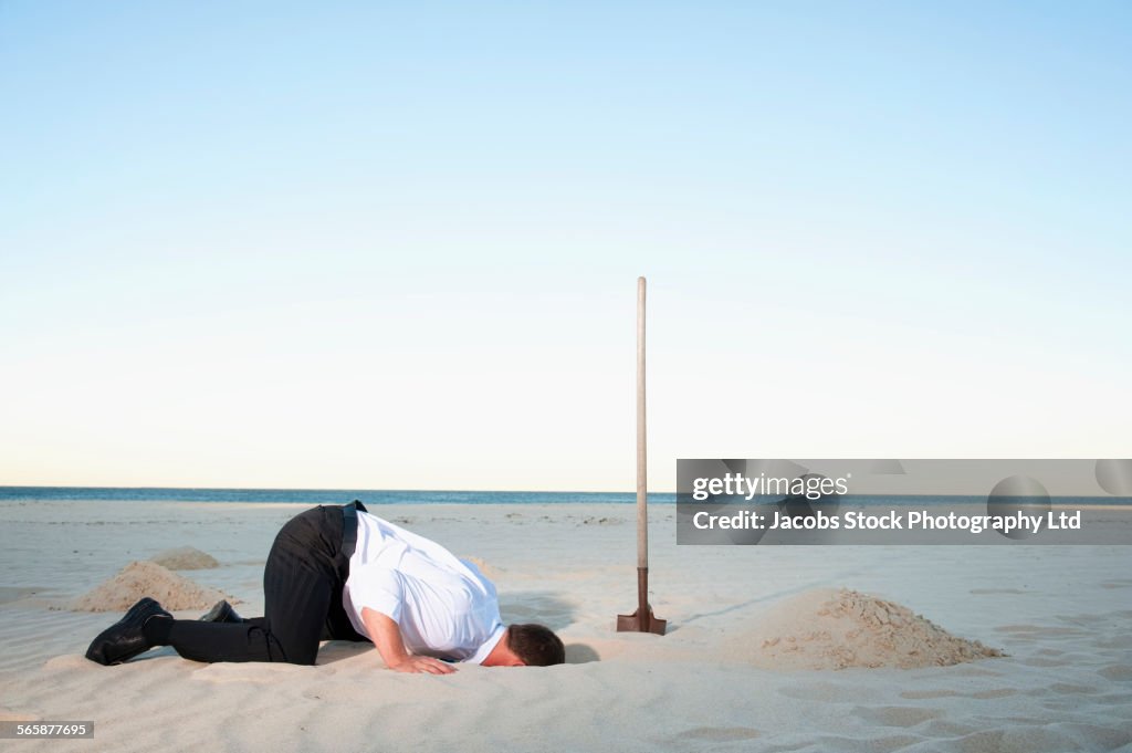 Caucasian businessman burying head in sand