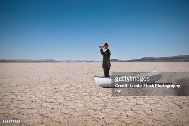 mixed race businessman in boat in dry desert landscape - spy glass businessman stock pictures, royalty-free photos & images
