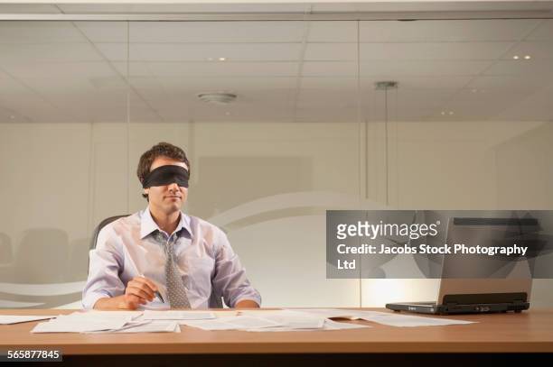 hispanic businessman wearing blindfold in office - blinddoek stockfoto's en -beelden