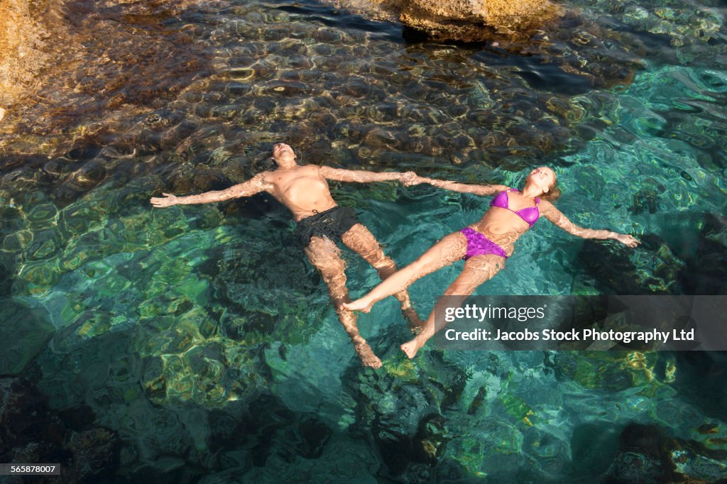 Couple floating and holding hands in ocean