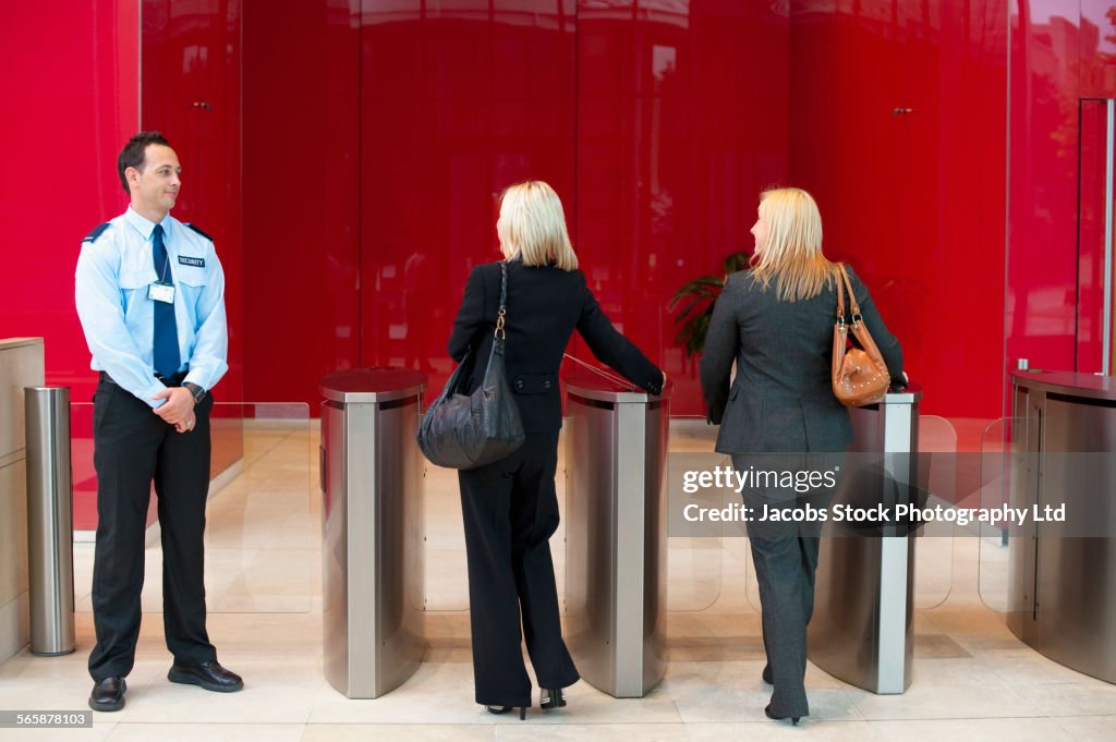 Businesswomen walking through turnstiles near security guard