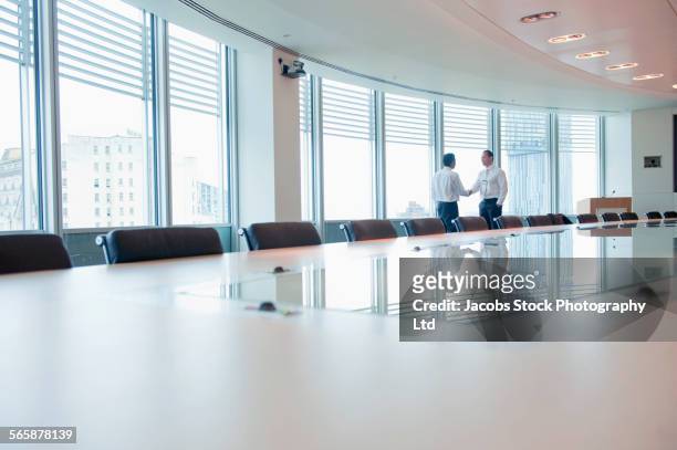 businessmen shaking hands near window in office conference room - deal england stock-fotos und bilder