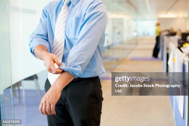 caucasian businessman rolling up sleeves in office - sleeve roll stock pictures, royalty-free photos & images