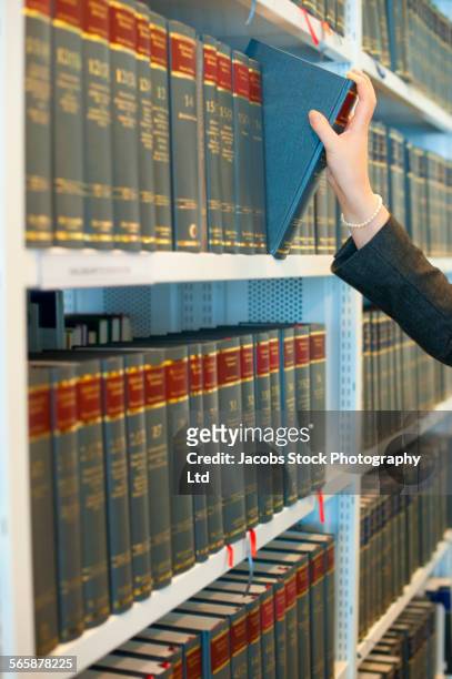 caucasian businesswoman pulling book from law library shelf - law books fotografías e imágenes de stock