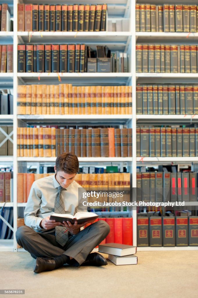 Caucasian businessman reading on floor in law library