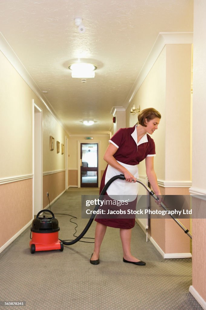 Caucasian maid vacuuming hotel hallway