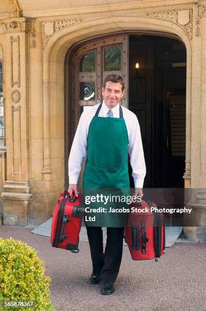 caucasian butler carrying luggage outside hotel - carry on luggage photos et images de collection