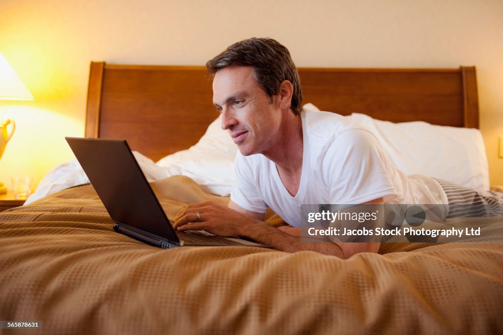 Caucasian man using laptop on hotel bed