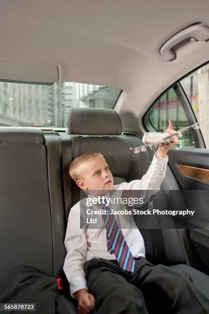 caucasian boy in suit playing with toy airplane in back seat of car - child prodigy foto e immagini stock