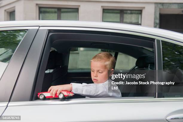 caucasian boy playing with toy car in back seat - child prodigy foto e immagini stock