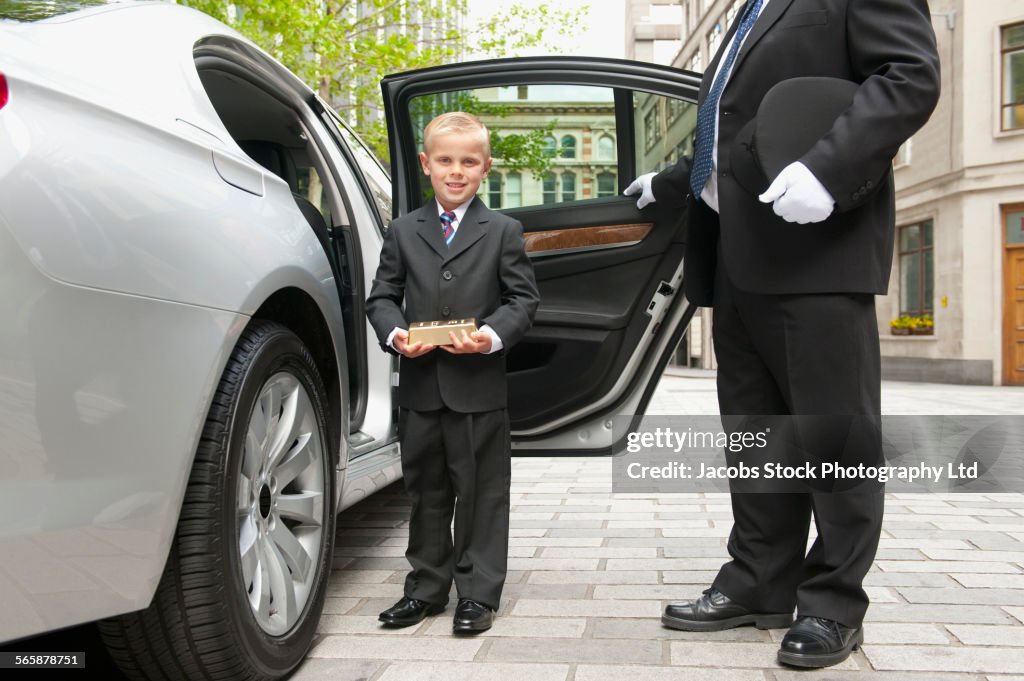 Caucasian driver opening car door for businessman boy
