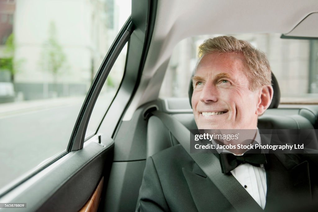 Caucasian man wearing tuxedo in back seat of car