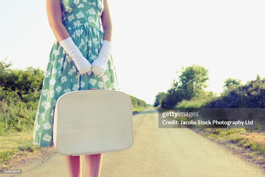 Caucasian woman carrying luggage on rural road