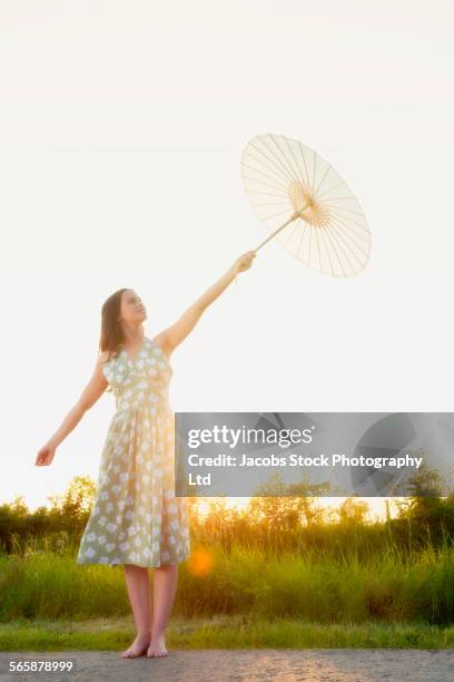 caucasian woman holding parasol on rural road - spalding place stock-fotos und bilder