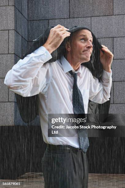 caucasian businessman covering head with suit jacket in rain storm - bad luck 個照片及圖片檔