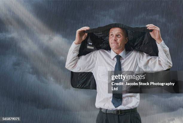 caucasian businessman covering head with suit jacket in rain storm - suit jacket stock pictures, royalty-free photos & images
