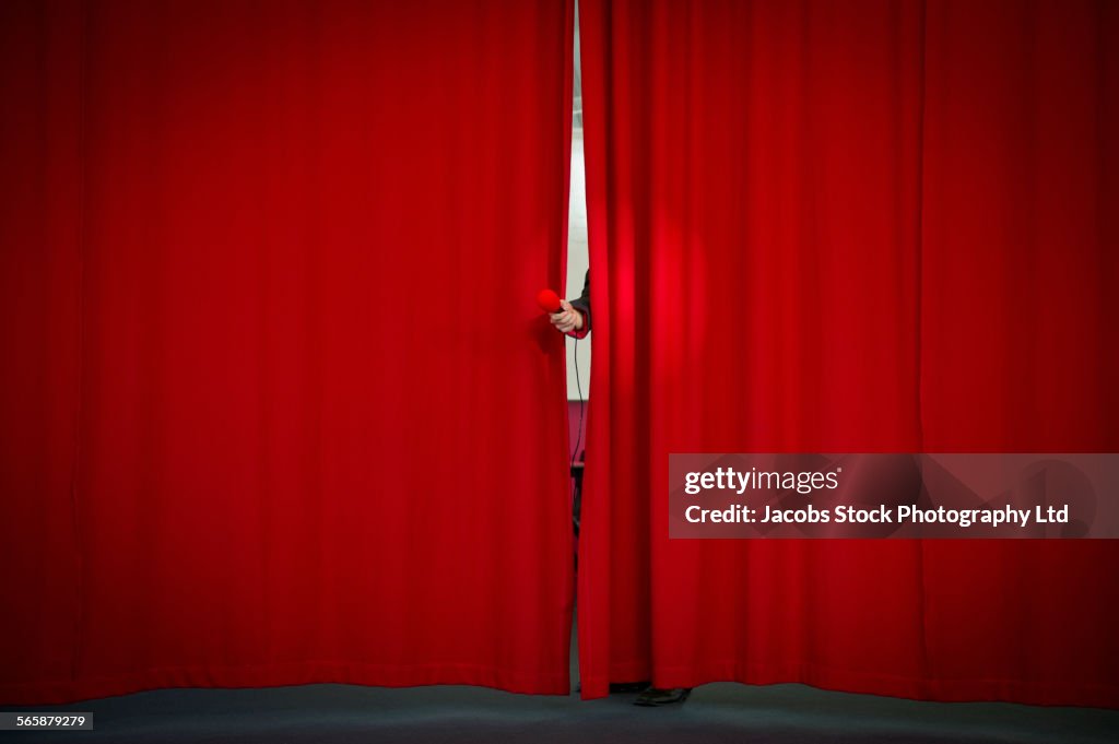 Caucasian businessman holding microphone from behind curtain