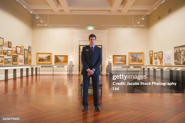 caucasian security guard standing in art museum - usciere foto e immagini stock