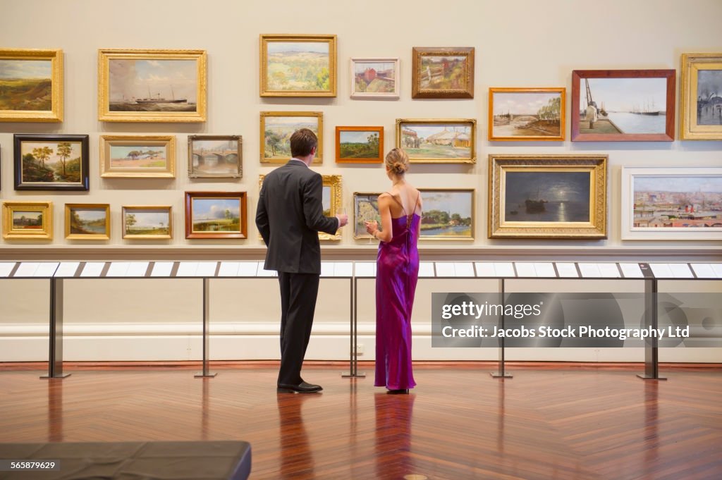 Caucasian couple in evening wear admiring art in museum