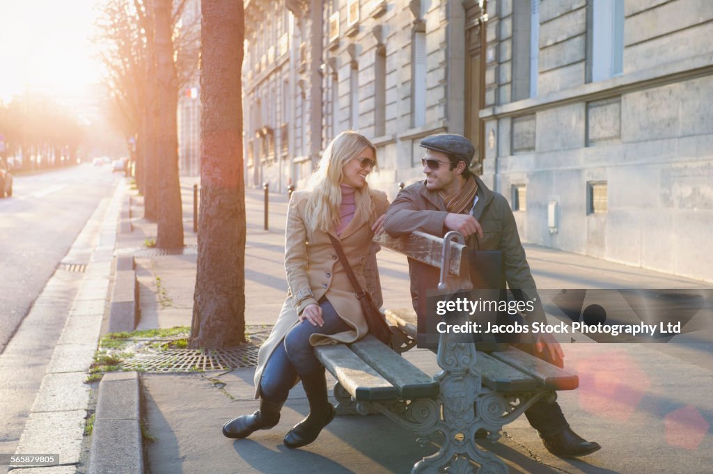 Caucasian couple sitting on benches on city sidewalk