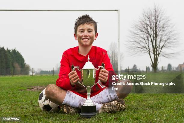 dirty caucasian boy holding trophy on soccer field - solo bambini maschi foto e immagini stock