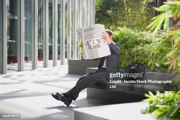 caucasian businessman reading newspaper in urban park - viso nascosto foto e immagini stock