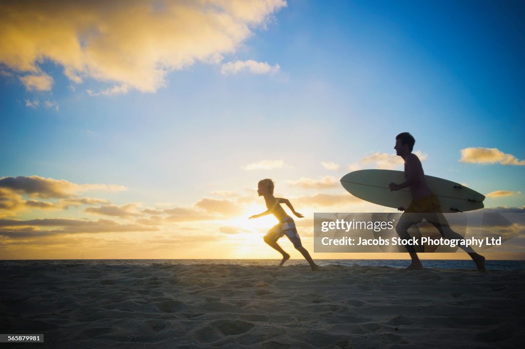 Caucasian father and son running with surfboard on beach