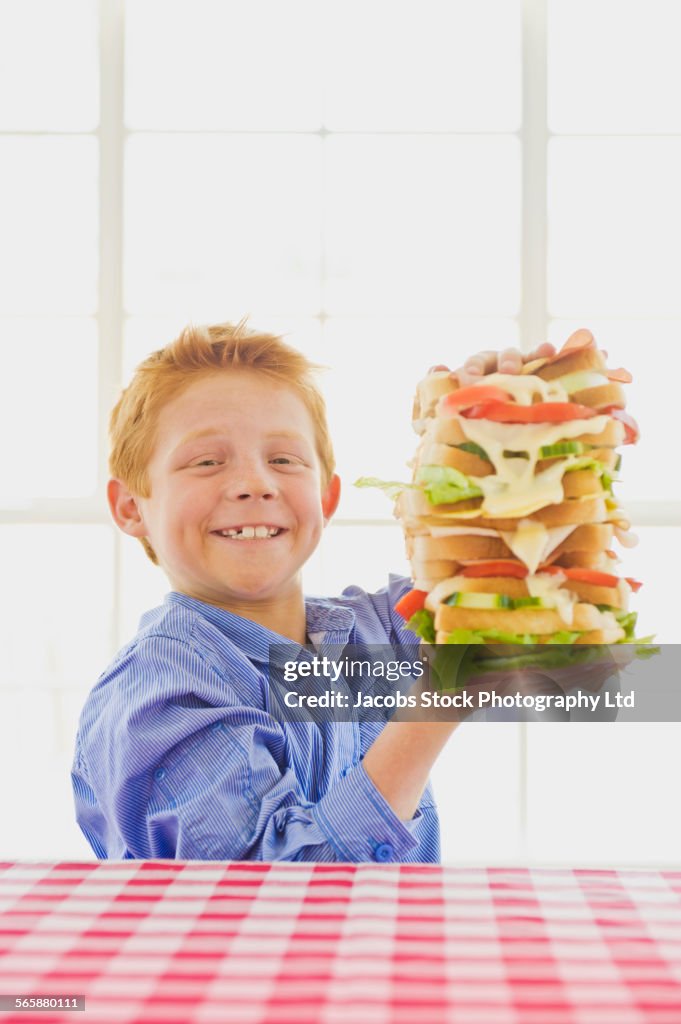 Caucasian boy holding tall sandwich on table