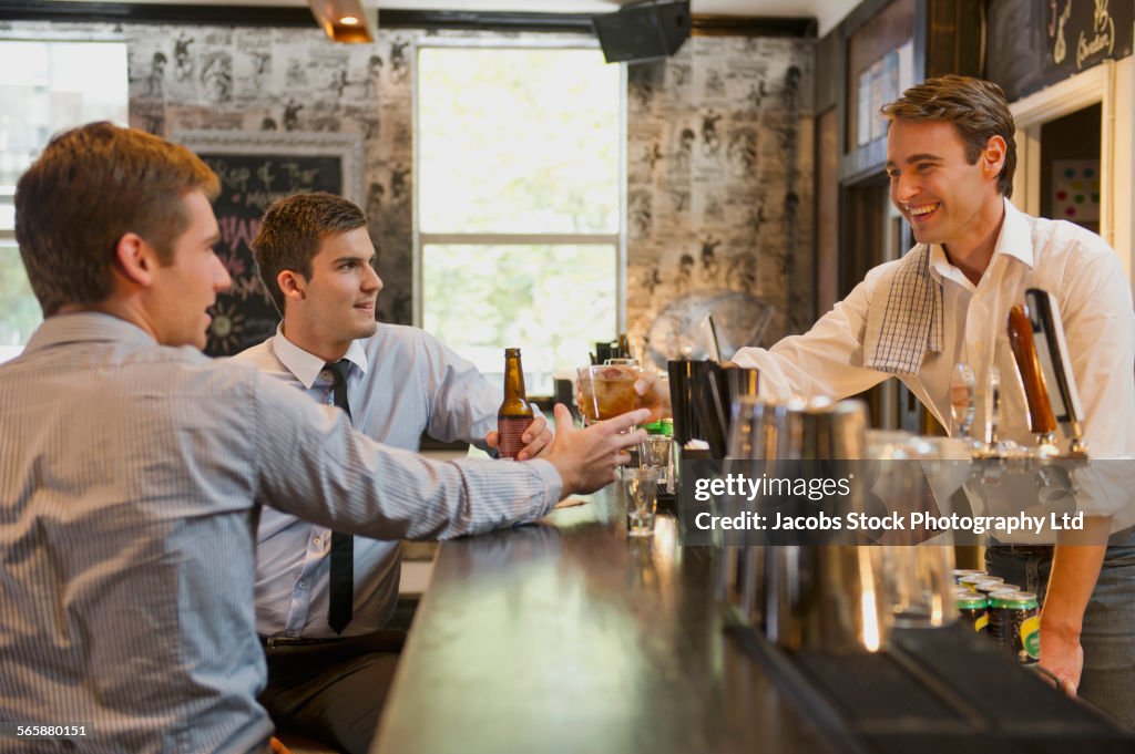 Businessmen talking to bartender and drinking at bar