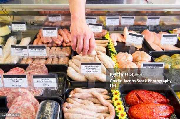 caucasian butcher selecting sausage from cooler in shop - spalding england stock pictures, royalty-free photos & images