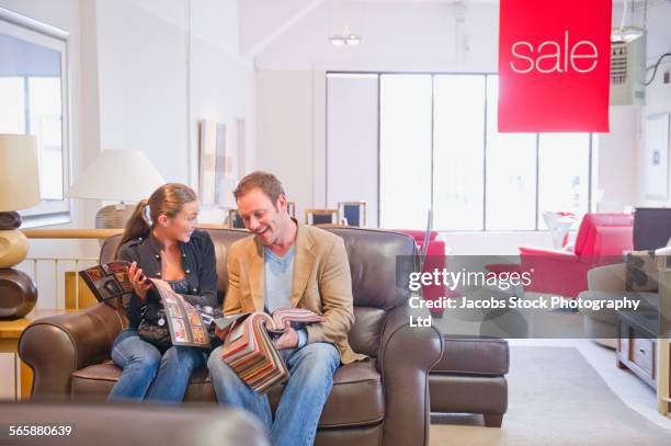 caucasian couple examining fabric swatches in furniture store - woman sitting on mans lap stockfoto's en -beelden