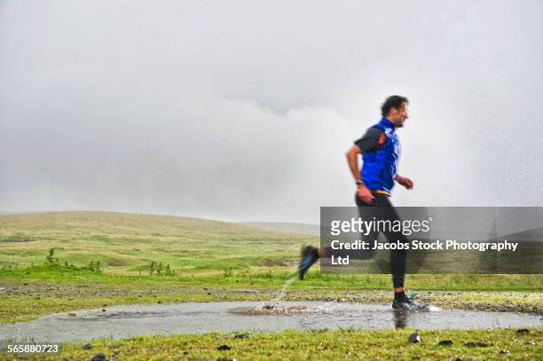 Caucasian man jogging in puddle in rural field
