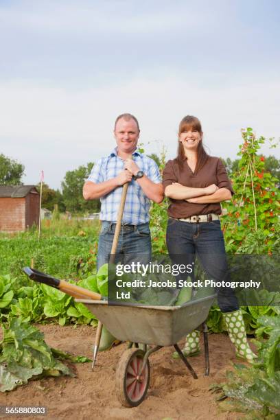 caucasian farming couple with wheelbarrow of vegetables - spalding place stock-fotos und bilder