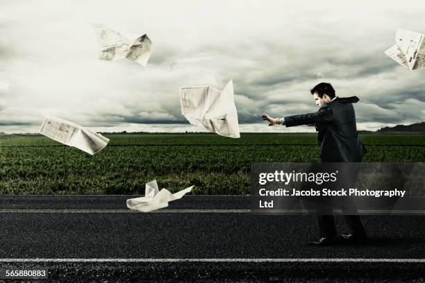 caucasian businessman with newspaper on windy remote road - paper blowing stock pictures, royalty-free photos & images