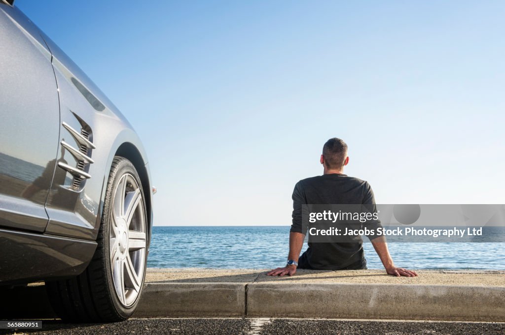 Hispanic man admiring beach near car in parking lot