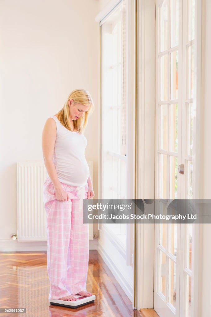 Pregnant Caucasian woman checking weight on scale