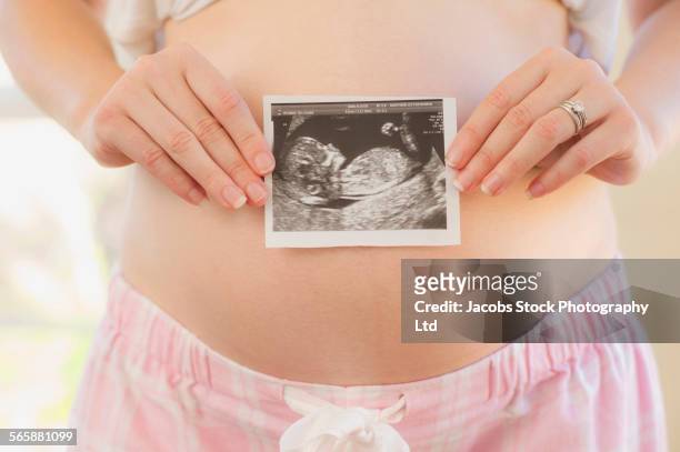 caucasian woman holding sonogram over pregnant belly - prenatal care stock pictures, royalty-free photos & images