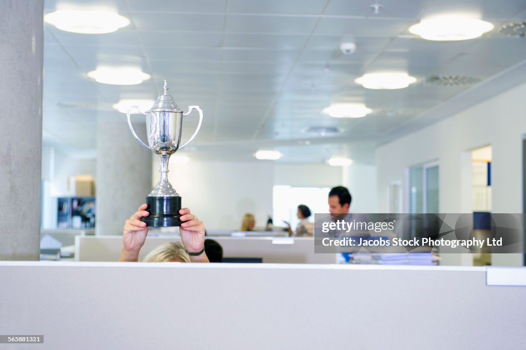 Businesswoman holding trophy over office cubicle