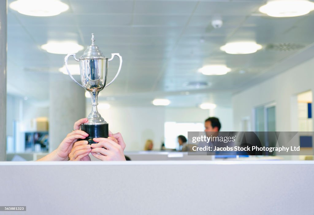 Businesswoman holding trophy over office cubicle