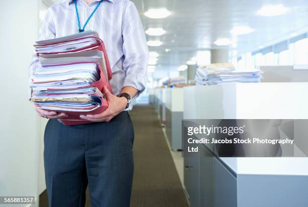 caucasian businessman carrying paperwork in office - papierstapel stock-fotos und bilder