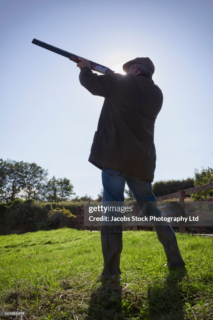 Caucasian man aiming shotgun in rural field