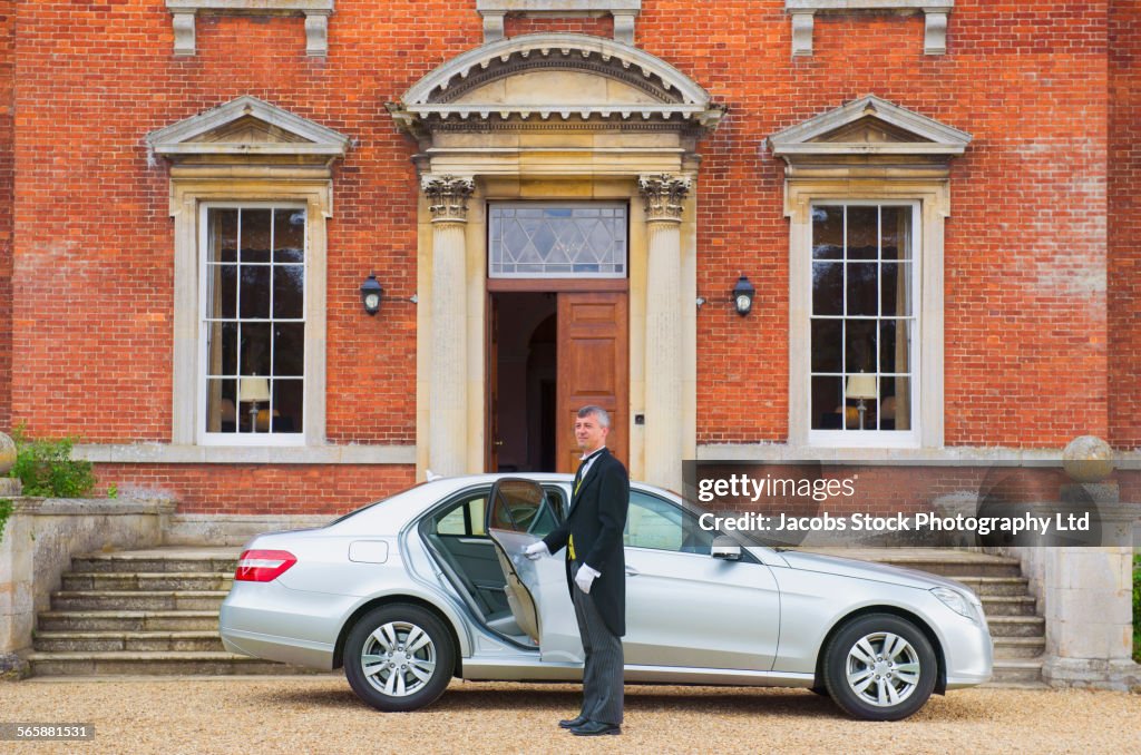 Caucasian butler opening car door outside mansion