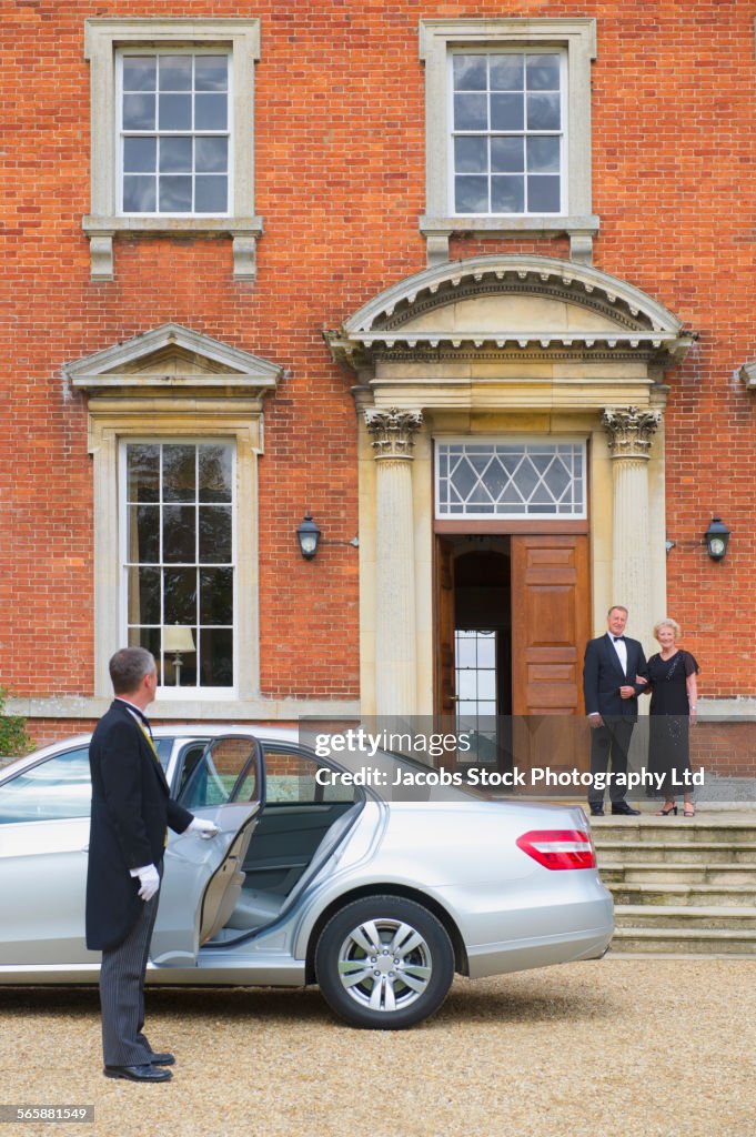 Caucasian butler opening car door for couple outside mansion
