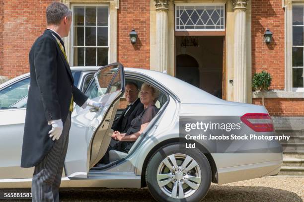 caucasian butler opening car door for couple outside mansion - car door stock pictures, royalty-free photos & images