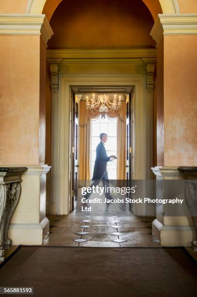 caucasian butler carrying tray in mansion hallway - buttler stock-fotos und bilder