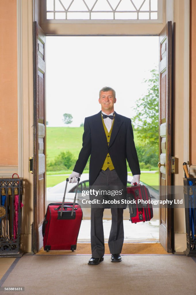 Caucasian butler rolling luggage in mansion front door